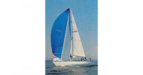 Photograph of Morning Cloud under full sail. The crew member standing by the mast is controlling the blue spinnaker.
